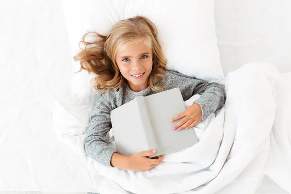 Ansicht von oben glückliches blondes Mädchen im Bett liegend mit grauem Buch, looki — Stockfoto