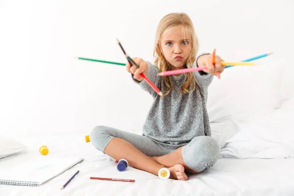 Lustiges kleines Mädchen im grauen Pyjama, das mit bunten Bleistiften spielt, — Stockfoto
