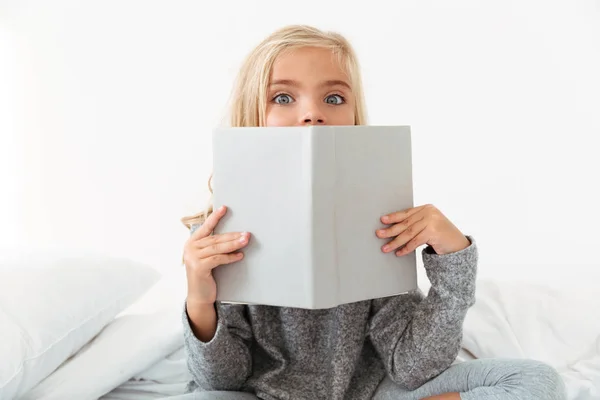 Nahaufnahme Porträt eines charmanten Mädchens, das sein Gesicht mit Buch bedeckt, — Stockfoto