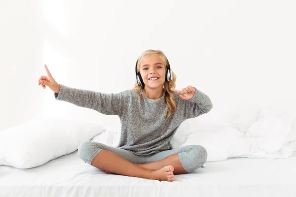 Fille blonde joyeuse en pyjama gris écoutant de la musique et danc — Photo