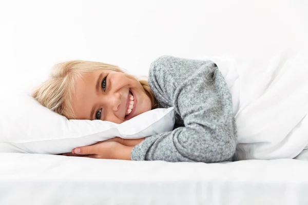 Крупный план портрета смеющейся маленькой девочки, лежащей на кровати с рукой — стоковое фото