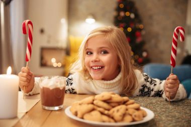 Sevimli sarışın çocuk şenlikli masada oturan iki şekerler ile