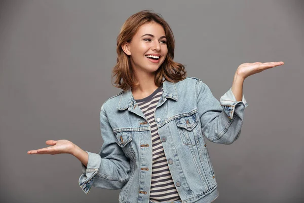 Jovem mulher alegre em jaqueta jeans olhando para a palma vazia — Fotografia de Stock