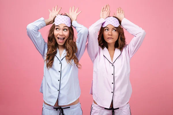ピンクの背景に分離されたパジャマで面白い 2 人の女性友達 — ストック写真