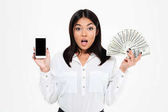 schockierte junge asiatische Frau mit Geld zeigt Anzeige des Telefons.
