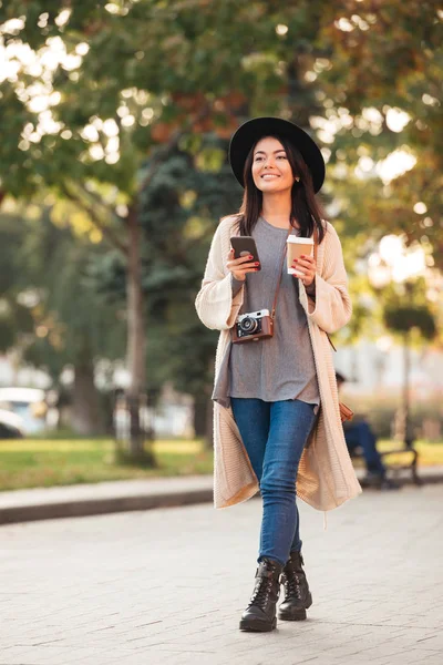 Moderna mulher asiática segurando telefone celular e xícara de café, enquanto wal — Fotografia de Stock