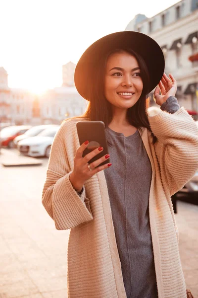 Charmoso na moda mulher asiática em chapéu preto segurando telefone celular em — Fotografia de Stock