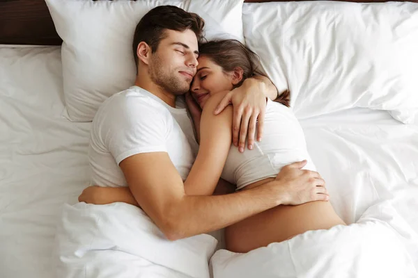 Gravid kvinna sover i sängen med maken — Stockfoto