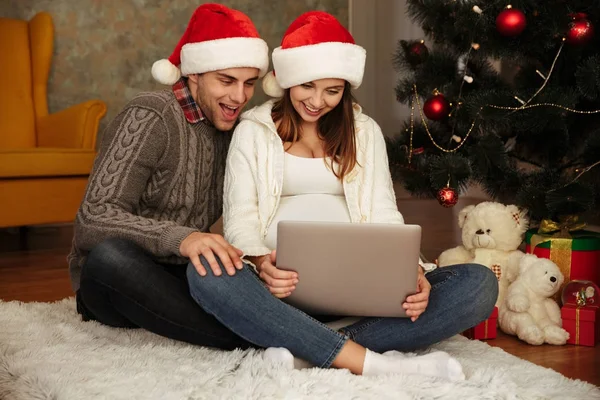 Feliz pareja joven en sombreros de Navidad sentados en el suelo —  Fotos de Stock