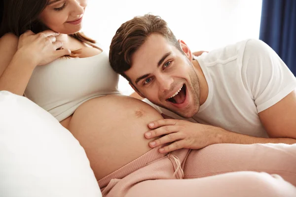 Счастливый молодой человек слушает живот беременной жены — стоковое фото
