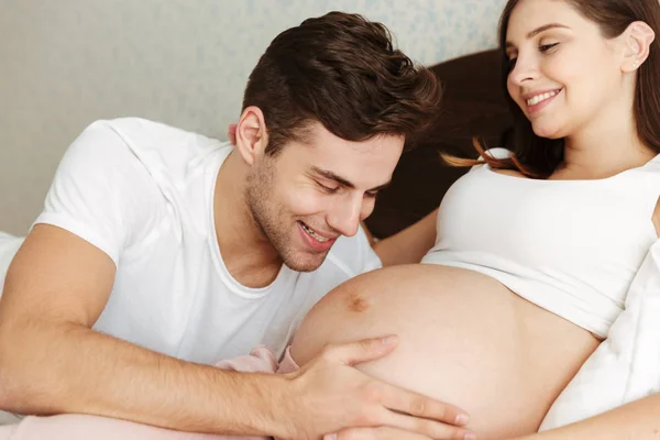 Счастливая беременная жена лежит в постели со своим мужем — стоковое фото