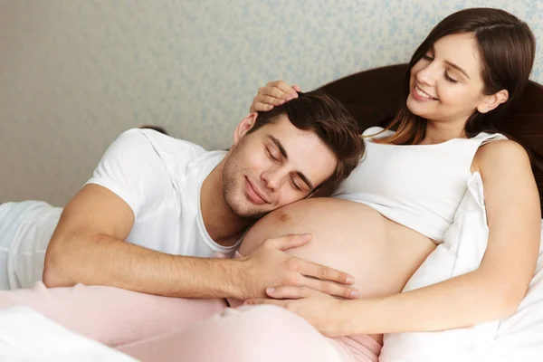 Lachende jonge zwangere vrouw liggend in bed met haar echtgenoot — Stockfoto