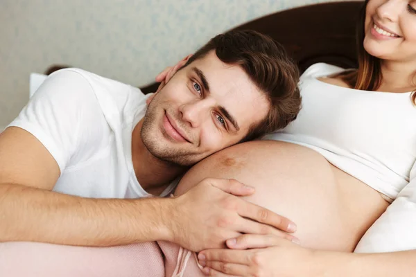 Jovem mulher grávida feliz deitada na cama com o marido — Fotografia de Stock