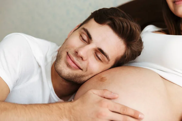 Gelukkig jonge man liggen op de buik van zijn zwangere wifes — Stockfoto