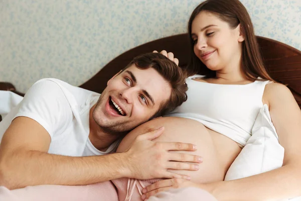 Satisfeita jovem esposa grávida deitada na cama com o marido — Fotografia de Stock