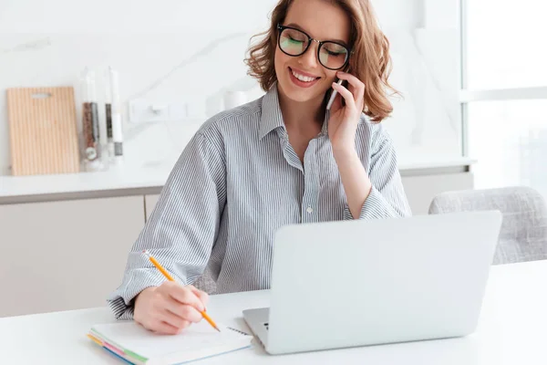 Retrato de bela mulher sorridente em óculos tomando notas enquanto — Fotografia de Stock