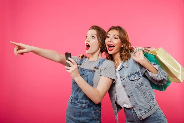 Emocionado dos amigas sosteniendo bolsas de compras usando teléfono móvil . — Foto de Stock