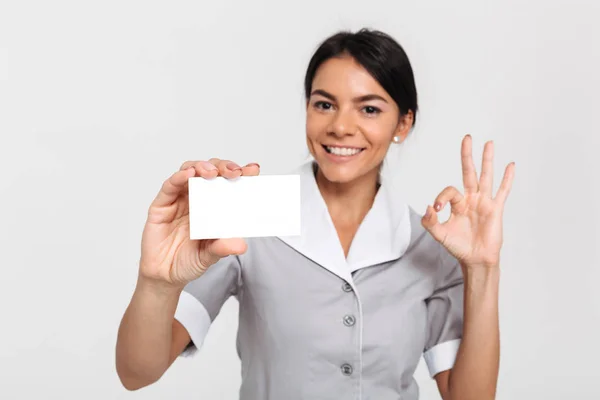 Portrait of happy maid in uniform showing empty sign card and OK — Stock Photo, Image