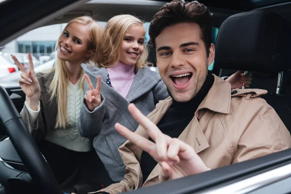 Feliz joven familia sentada en coche mostrando gesto de paz —  Fotos de Stock