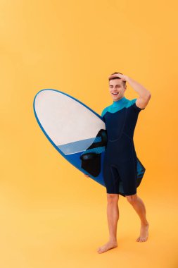 Tam boy görüntü surfboard ile yürüyen genç gülümseyen sörfçü