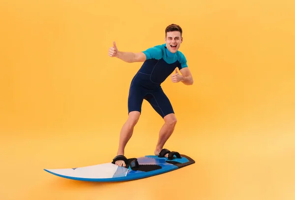 Foto van vrolijke surfer in wetsuit met behulp van surfplank — Stockfoto