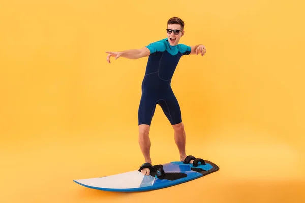 Foto van gelukkig surfer in wetsuit en zonnebril met behulp van surfplank — Stockfoto