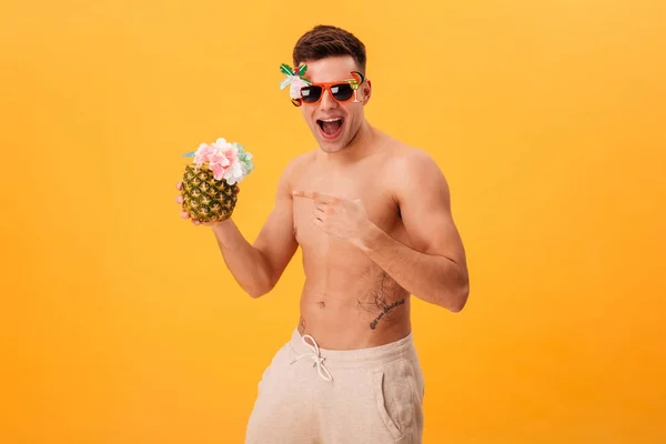 Cheerful naked man in shorts and unusual sunglasses holding cocktail — Stock Photo, Image