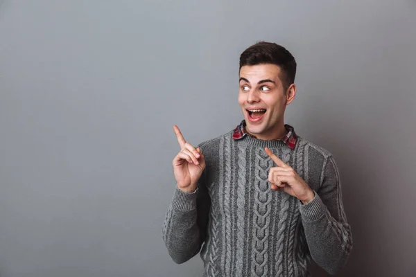 Surprised happy brunette man in sweater pointing and looking aside — Stock Photo, Image