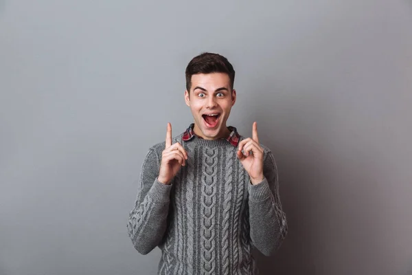 Surprised happy brunette man in sweater pointing up — Stock Photo, Image