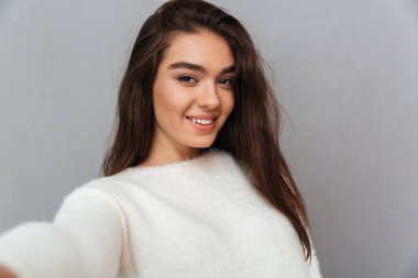 Genç güzel gülümseyen kadın beyaz yumuşak kazaklı selfi alarak