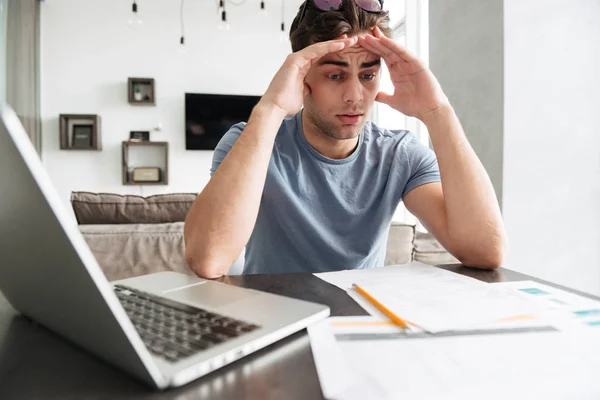 Homem concentrado confuso trabalhando com papéis e laptop — Fotografia de Stock