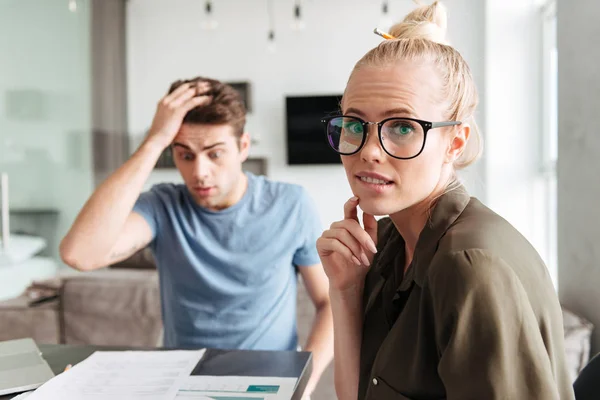 Femme confondue regardant caméra tout en travaillant avec son homme choqué à la maison — Photo