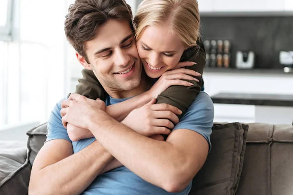 Glückliche schöne Frau umarmt ihren Mann, während sie auf dem Sofa sitzt — Stockfoto