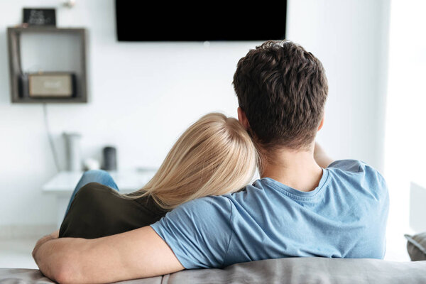 Вид сзади влюбленных, сидящих на диване и смотрящих телевизор
