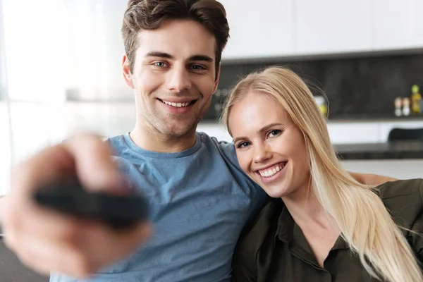 Porträt eines jungen Liebespaares, das auf dem Sofa sitzt und Fernbedienung in der Hand hält — Stockfoto