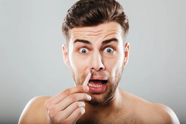 Scared man removing nose hair with tweezers