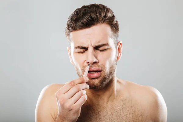 Man in pain removing nose hair with tweezers