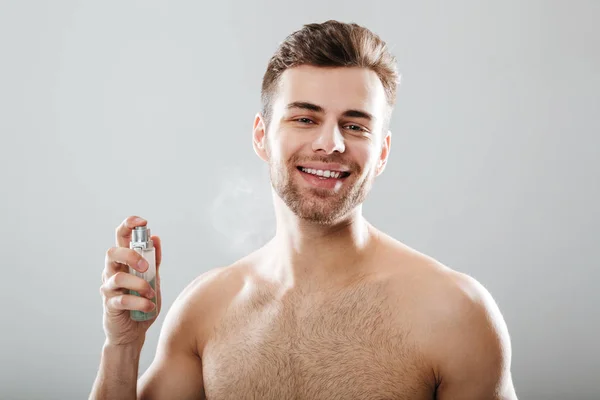 Retrato de um homem seminua sorridente pulverizando perfume — Fotografia de Stock