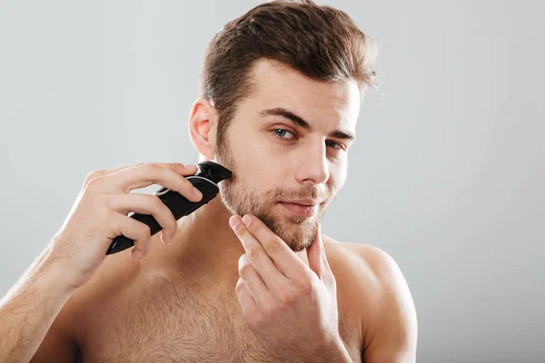 Retrato de homem bonito barbeando sua barba com barbeador elétrico — Fotografia de Stock