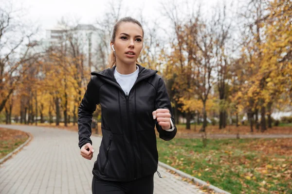 Retrato de una chica de fitness concentrada en auriculares corriendo — Foto de Stock