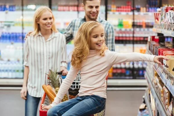 Niña sonriente sentada en un carrito de compras —  Fotos de Stock