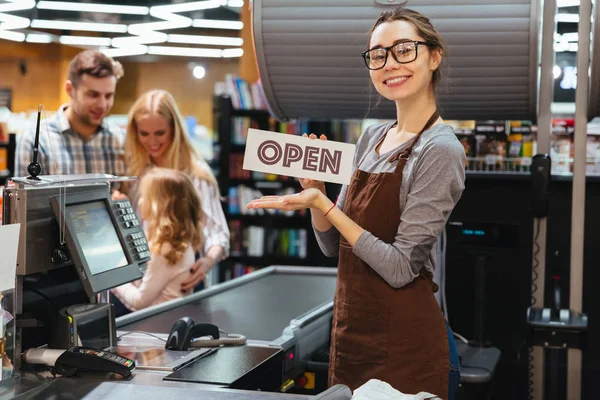 Portrait of happy woman cashier holding open sign — Stock Photo, Image