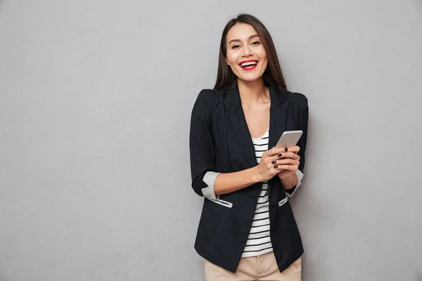 Glad asiatiska affärskvinna hålla smartphone och tittar på kameran — Stockfoto