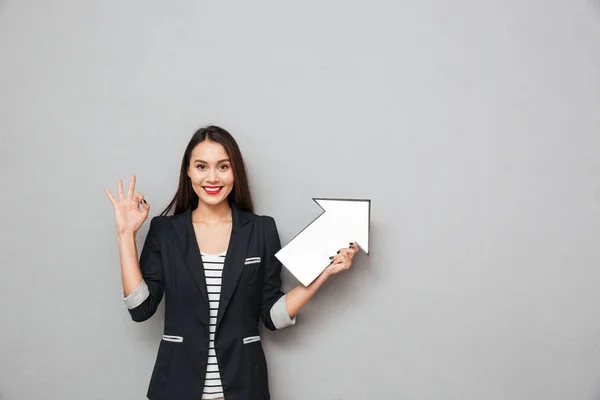 Усміхнена азіатська бізнес-леді показує знак і вказує — стокове фото