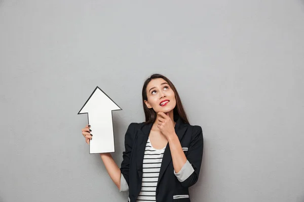 Nadenkend lachende Aziatische business woman wijzend met papier pijl — Stockfoto