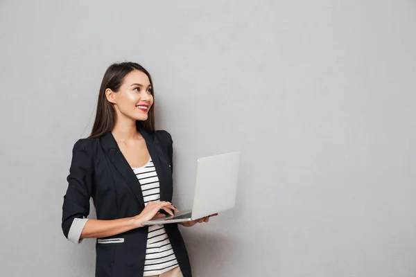Happy asian business woman holding laptop computer and looking away — Stock Photo, Image
