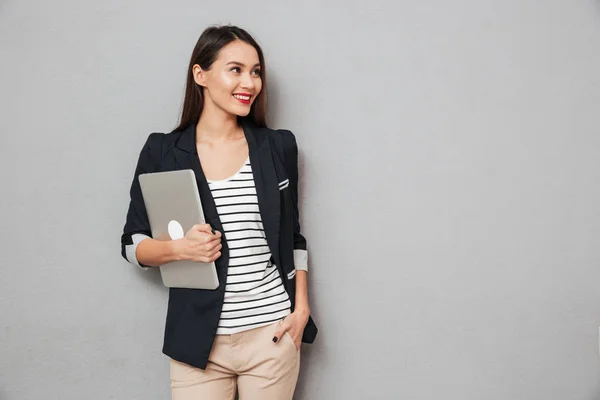 Счастливая деловая женщина с рукой в кармане держит ноутбук — стоковое фото