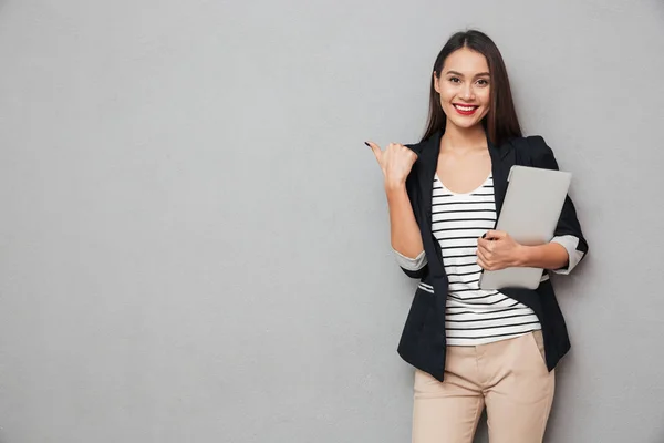 Lächelnde asiatische Geschäftsfrau hält Laptop in der Hand und zeigt weg — Stockfoto