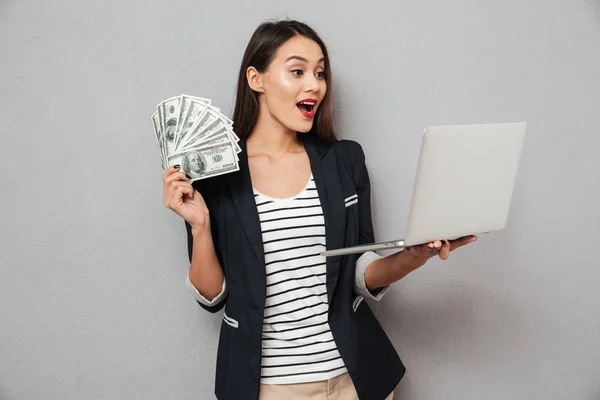 Surpreendido asiático mulher de negócios segurando dinheiro e laptop computador — Fotografia de Stock