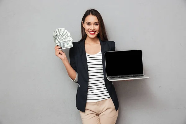 Mujer de negocios feliz mostrando computadora portátil en blanco y sosteniendo el dinero —  Fotos de Stock